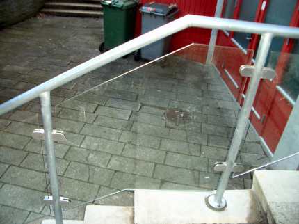 Trappeindgang gelænder rækværk, af galv. 42 mm Stålrør, med rustfri glasbeslag som holder for faconskåret lamineret sikkerhedsglas værn.